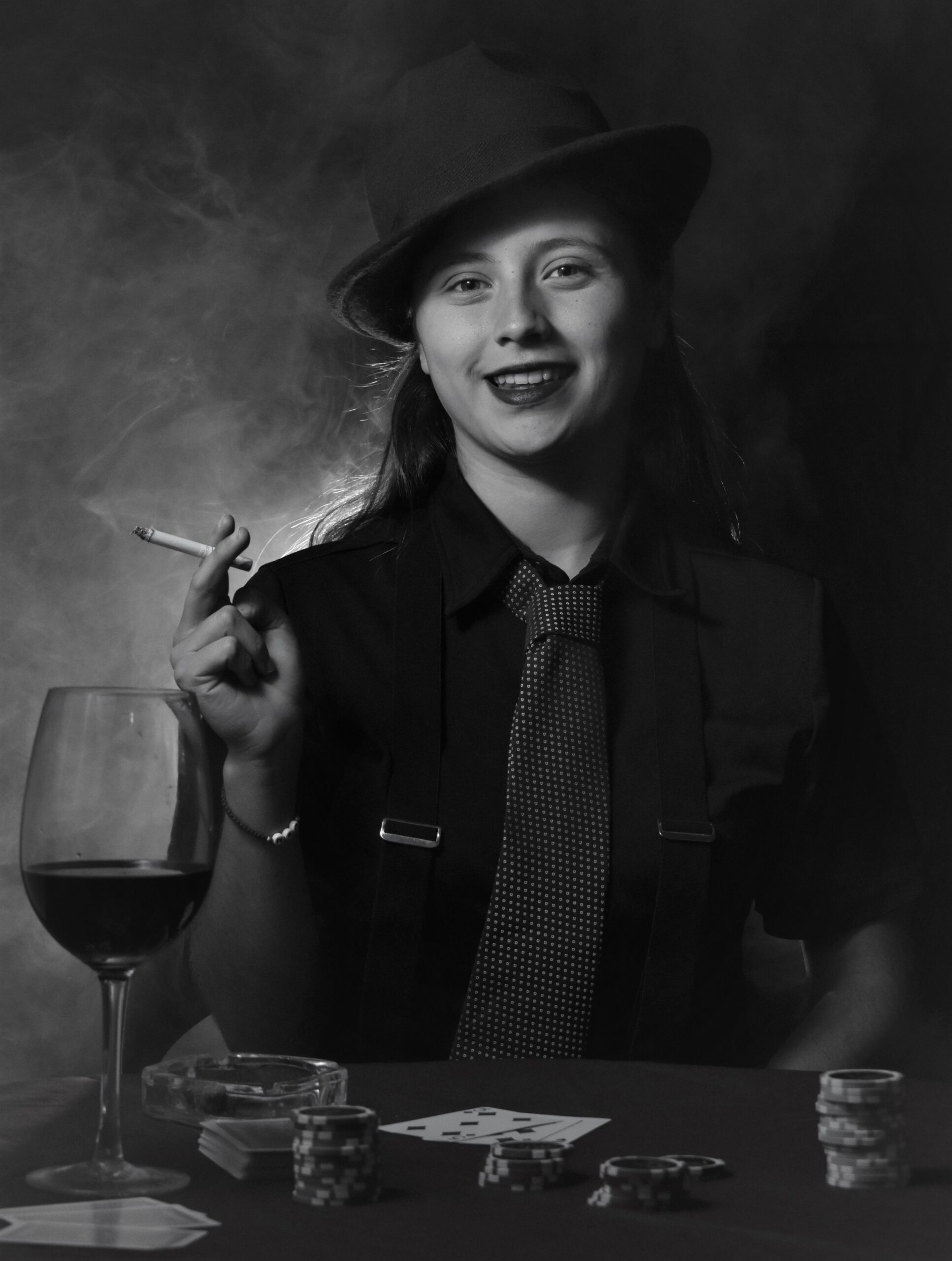 A stylish woman in vintage attire smokes and holds cards at a casino table.